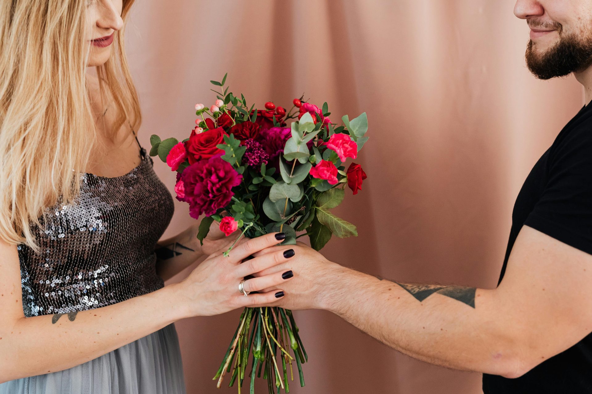 A man hands a vibrant flower bouquet to a woman in a sequined dress, creating a romantic mood.