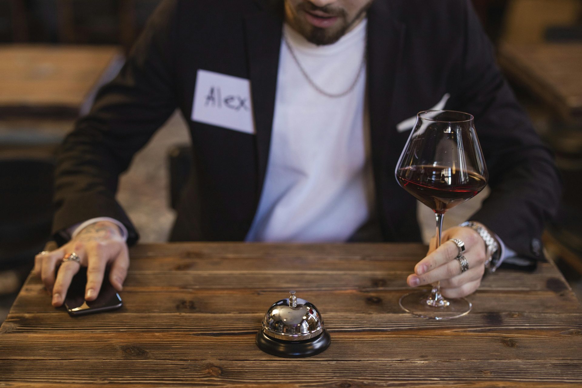 Adult man with wine glass and smartphone at a wooden table, evoking a speed dating ambiance.